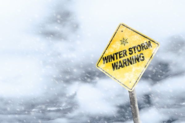 Yellow caution sign that says "Winter Storm Warning" in front of storm clouds
